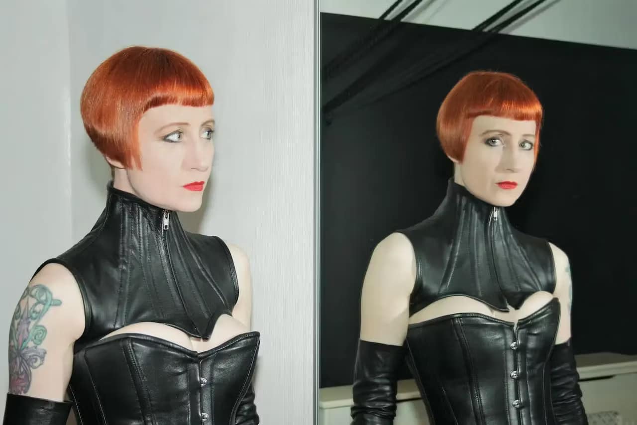 Domina Liza aus Derby in schwarzem Leder-Outfit vor einem Spiegel.