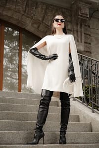 Domina Mistress Severna in weißem Cape-Kleid, schwarzen Lederhandschuhen und Overknee-Stiefeln auf einer Steintreppe.