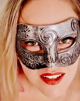 Switch Aglaya wearing an ornate silver mask in a close-up BDSM portrait