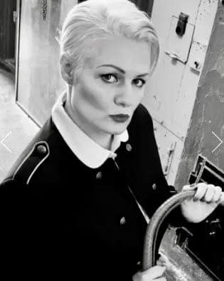 Frau Aufseherin in schwarz-weißer Aufnahme mit kurzer heller Frisur und Uniformlook.