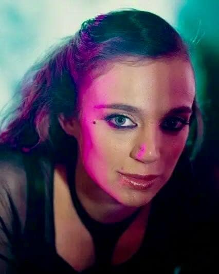 Female BDSM studio slave Usagi from Berlin in a close-up portrait with pink and turquoise lighting.
