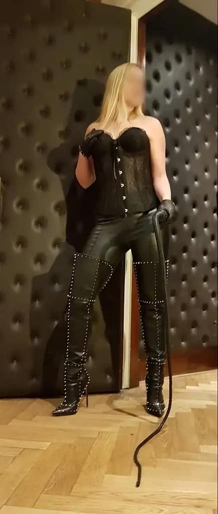 Miss Lynn Cane, niederländische Domina, in schwarzem Korsett, Lederhose und hohen Stiefeln mit Peitsche.