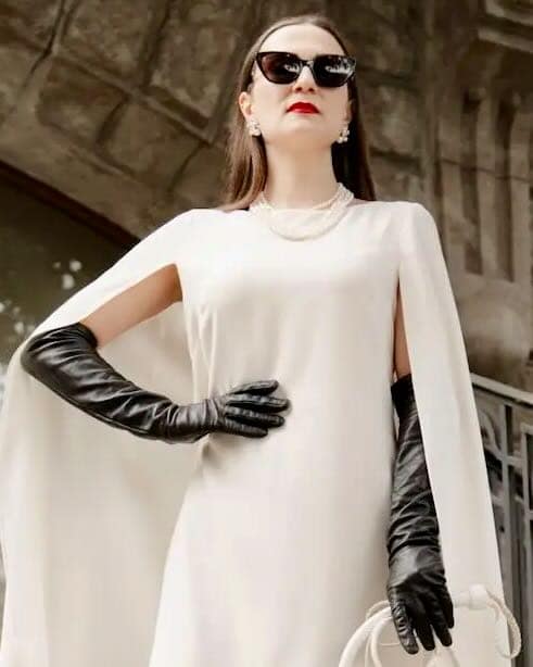 Mistress Severna, Lausanne-based Dominatrix, wearing an elegant white dress, black leather gloves, and sunglasses.