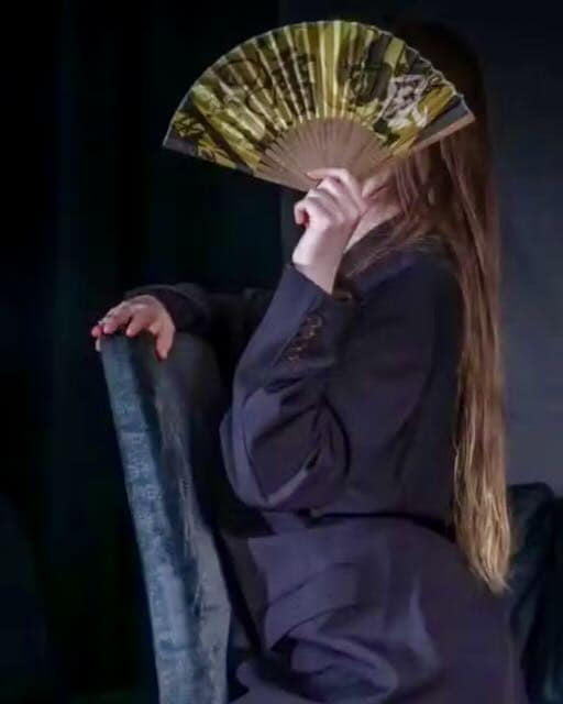 Lady Juna, Zurich dominatrix seated with a decorative fan covering her face