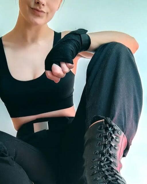 Woman in black BDSM attire with wrist wraps and lace-up boots