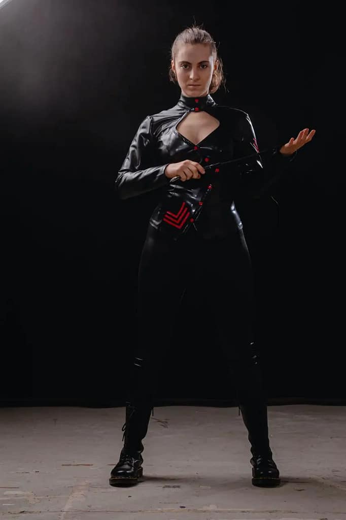 Dominatrix Miss Juli from Zurich, Switzerland, standing in a black latex outfit and holding a riding crop.