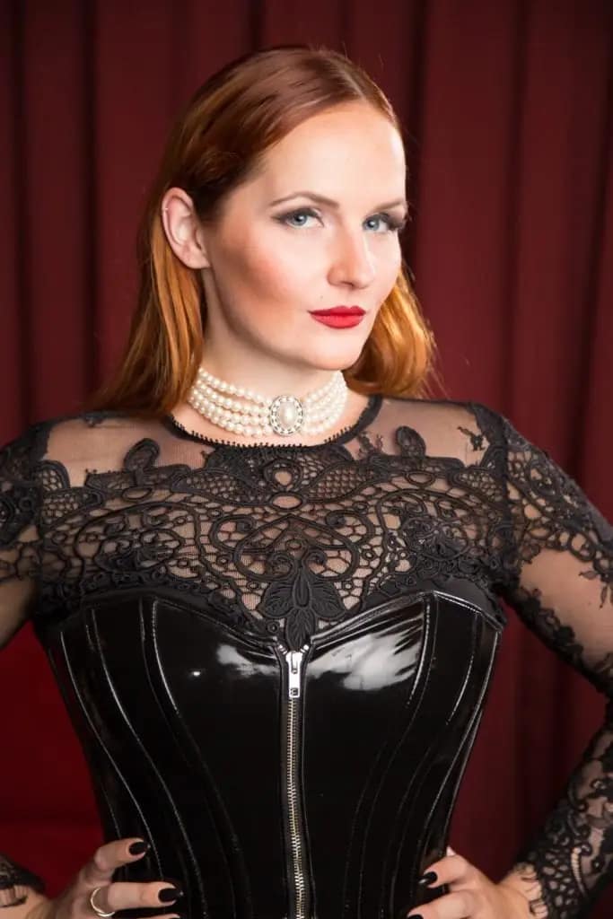 Cassandra van Cane, dominatrix from Zurich, wearing an elegant black corset and lace dress, looking confidently into the camera.