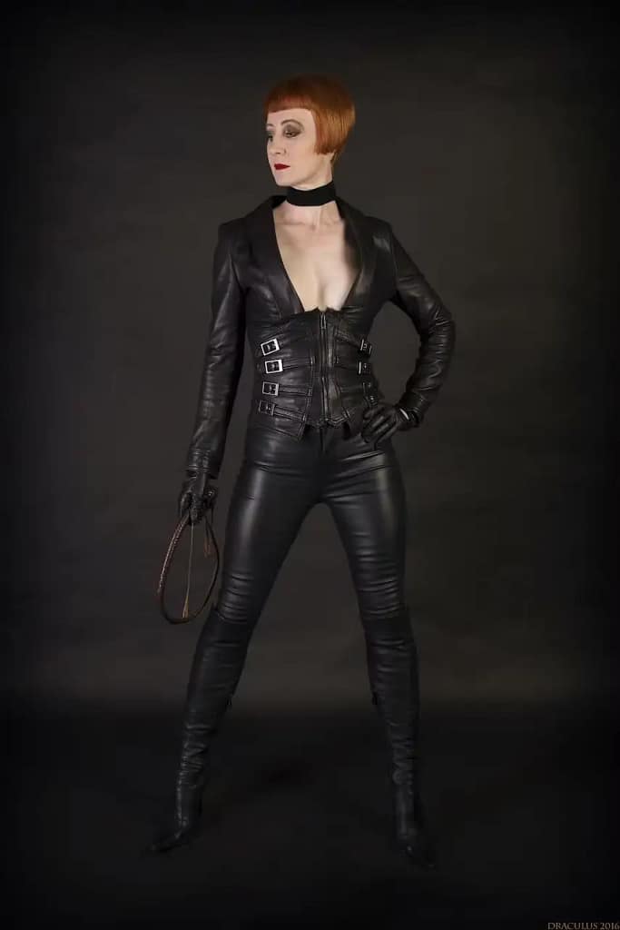Domina Liza, a dominatrix in Derby, United Kingdom, standing in black leather with a crop as an example of confident female dominance in BDSM.
