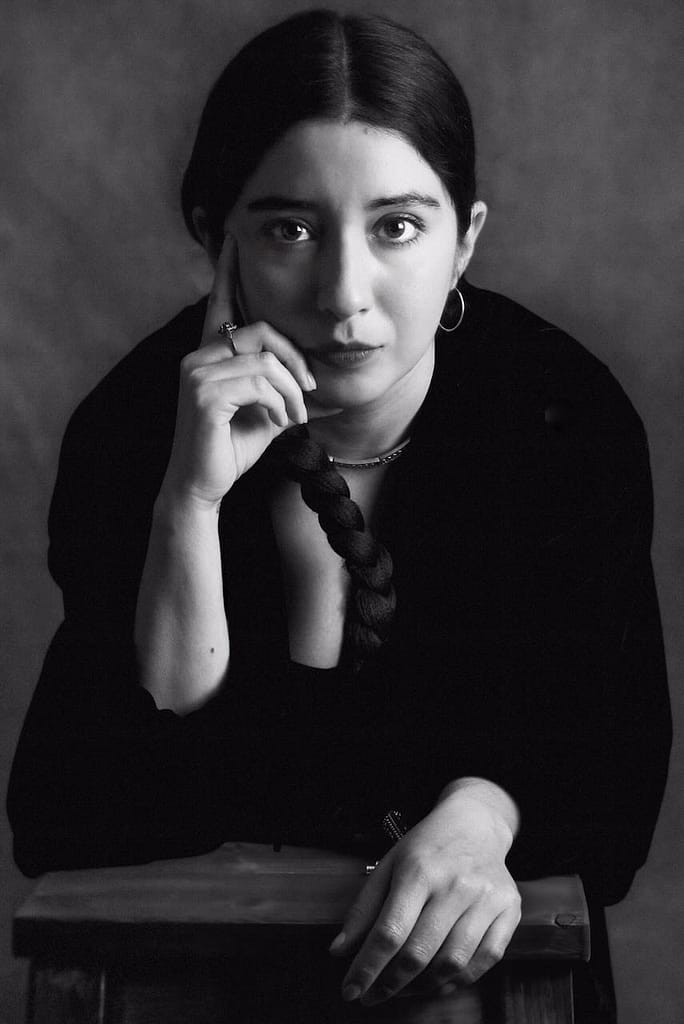 Black-and-white portrait of Mistress Leonor, a professional dominatrix in Barcelona, wearing a black blazer with her dark hair in a braid, looking directly at the camera.
