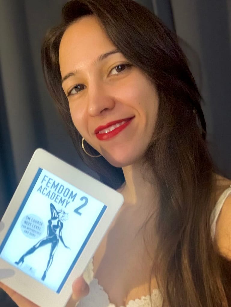 Domina Mistress Fun hält einen eBook-Reader mit dem Buch "Femdom Akademie 2" in der Hand.