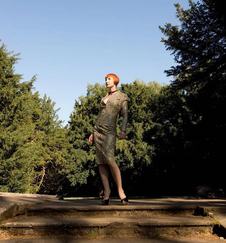 Domina Liza aus Derby steht in elegantem Outfit auf einer Treppe im Freien.